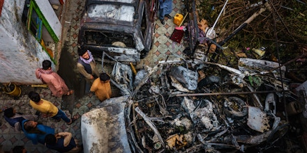 Relatives and neighbors of the Ahmadi family gather around the incinerated husk of their vehicle, targeted and hit by an American drone strike, in Kabul, Afghanistan, on Aug. 30, 2021.