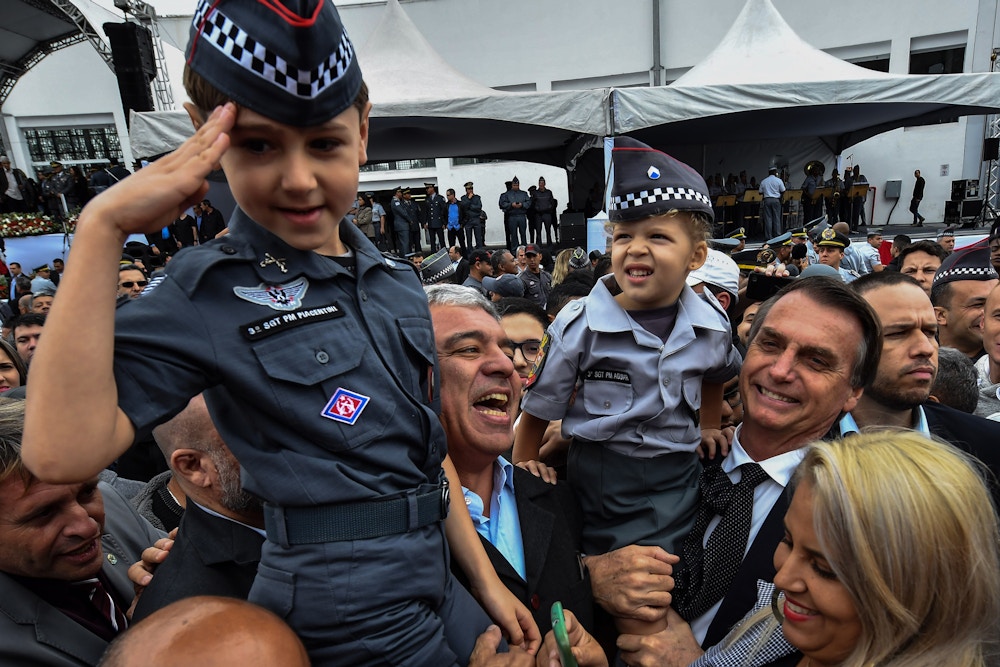 Brazilian presidential candidate for the Social Liberal Party (PSL) Jair Bolsonaro (R) holds a girl dressed in military uniform during the graduation ceremony of a military school in Sao Paulo, Brazil on August 17, 2018. - Brazilian general elections will take place next October 7. (Photo by NELSON ALMEIDA / AFP)        (Photo credit should read NELSON ALMEIDA/AFP via Getty Images)