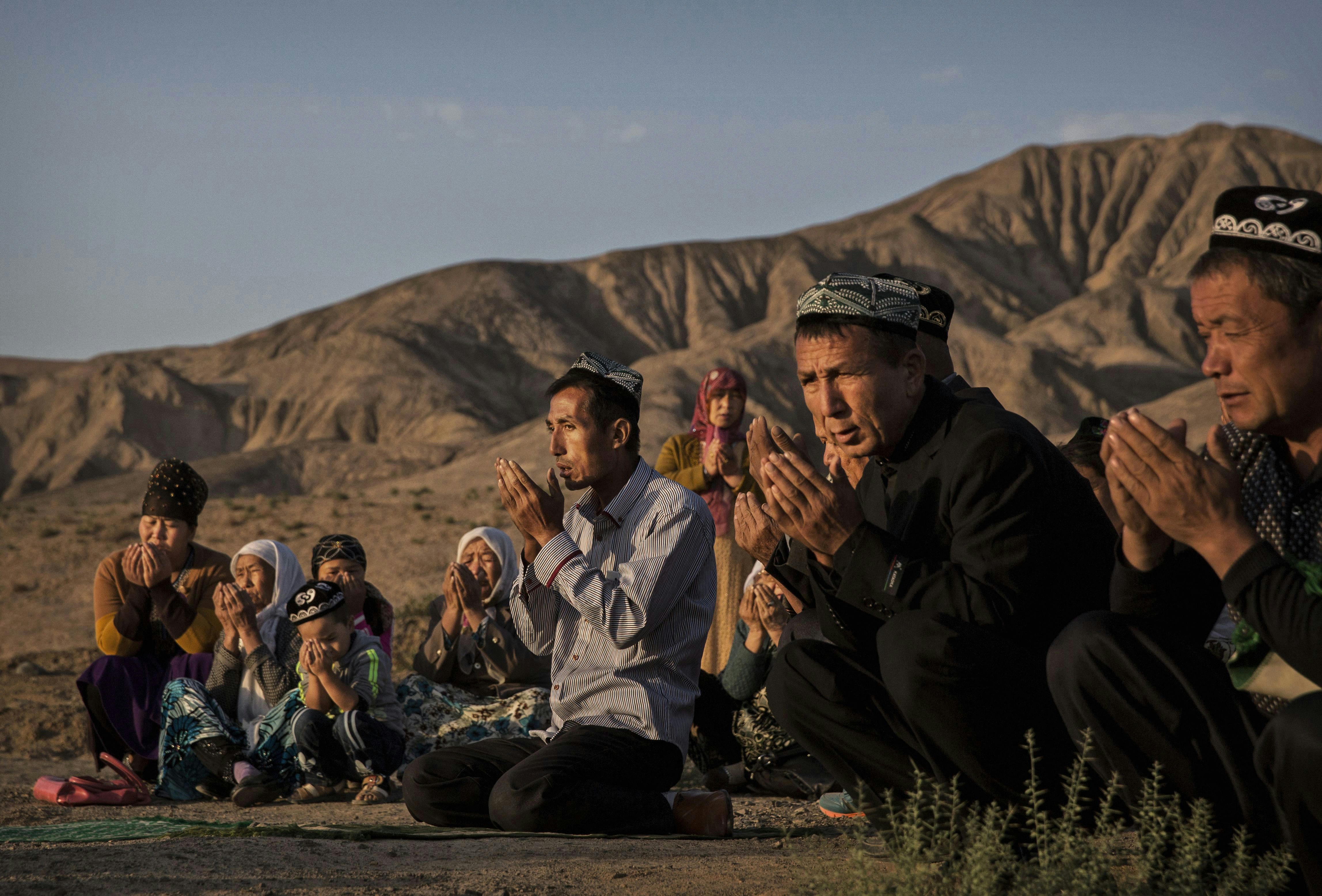 تورپان، چین - 12 سپتامبر: (خارج از چین) یک خانواده اویغور در صبح جشن کوربان در 12 سپتامبر 2016 در یک زیارتگاه و گورستان محلی در شهرستان تورپان، در غرب استان سین کیانگ، چین، بر سر مزار یکی از عزیزان خود دعا می کنند. .  قربان که برای مسلمانان سراسر جهان به عنوان عید قربان یا 