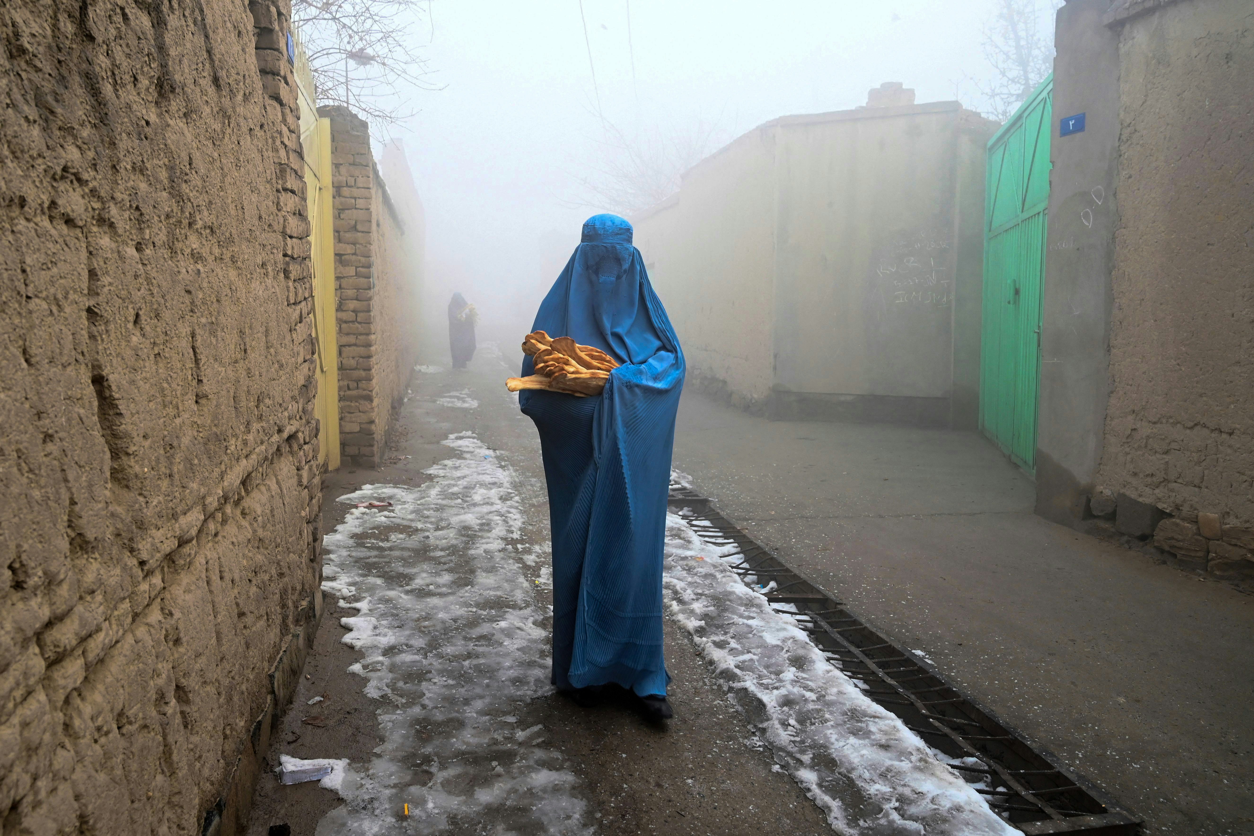 TOPSHOT - A woman wearing a burqa walks along a road towards her home after receiving free bread distributed as part of the Save Afghans From Hunger campaign in Kabul on January 18, 2022. (Photo by Wakil KOHSAR / AFP) (Photo by WAKIL KOHSAR/AFP via Getty Images)