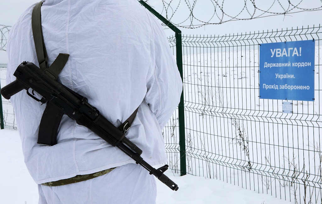 An armed border guard stands before a fence at the Ukraine-Russia border, Kharkiv Region, northeastern Ukraine, February 16, 2022.