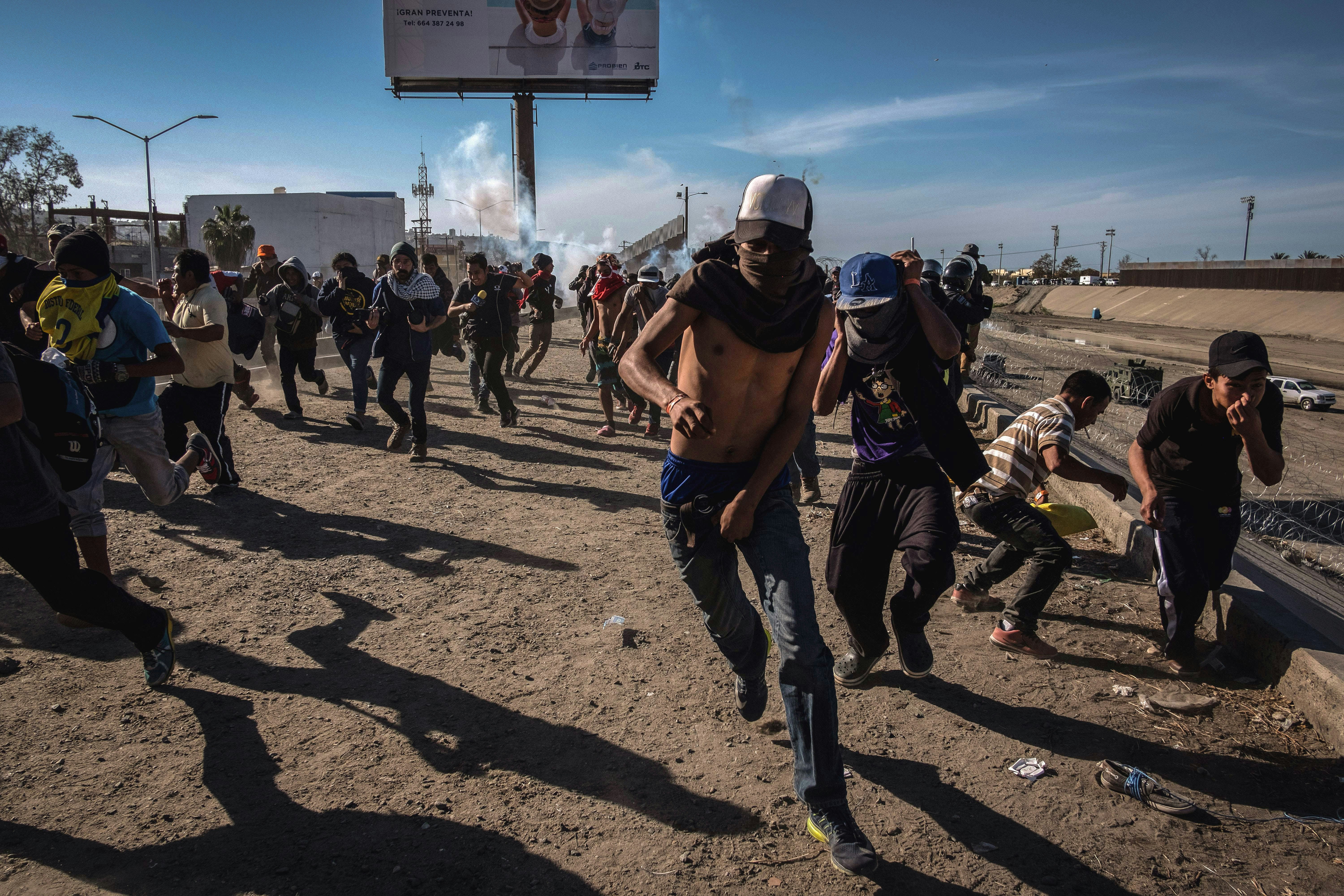 TOPSHOT - Central American migrants -mostly Hondurans- run along the Tijuana River near the El Chaparral border crossing in Tijuana, Baja California State, Mexico, near US-Mexico border, after the US border patrol threw tear gas from the distance to disperse them after an alleged verbal dispute, on November 25, 2018. - US officials closed the San Ysidro crossing point in southern California on Sunday after hundreds of migrants, part of the "caravan" condemned by President Donald Trump, tried to breach a fence from Tijuana, authorities announced. (Photo by GUILLERMO ARIAS / AFP)        (Photo credit should read GUILLERMO ARIAS/AFP via Getty Images)