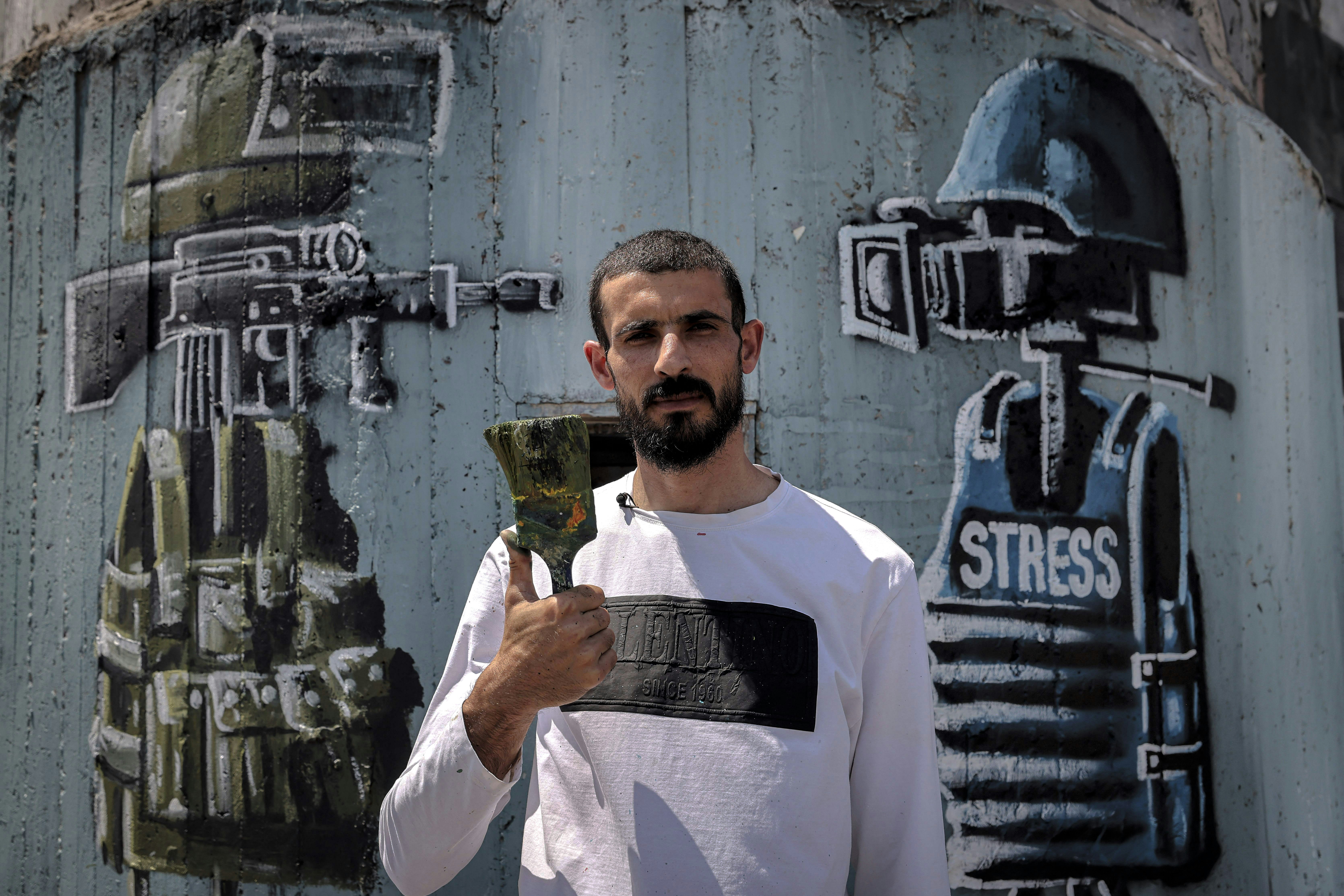 Palestinian artist Taqi Spateen poses for a photo before his mural depicting a sniper rifle underneath Jerusalem's Dome of the Rock facing a video camera wearing a press helmet and bulletproof vest labelled "stress", his latest creation on the theme of violence against journalists covering the Israeli-Palestinian conflict, on a section of Israel's controversial separation barrier in Bethlehem on June 30, 2021. (Photo by Emmanuel DUNAND / AFP) (Photo by EMMANUEL DUNAND/AFP via Getty Images)