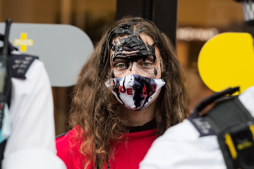 LONDON, UNITED KINGDOM - AUGUST 24, 2021: An environmental activist from Extinction Rebellion with face covered in fake oil protests outside Selfridges department store in Oxford Street against fashion industry's reliance on synthetic polyester and nylon textiles made from petroleum amid climate crisis and ecological emergency on 24 August 2021 in London, England. (Photo credit should read Wiktor Szymanowicz/Future Publishing via Getty Images)