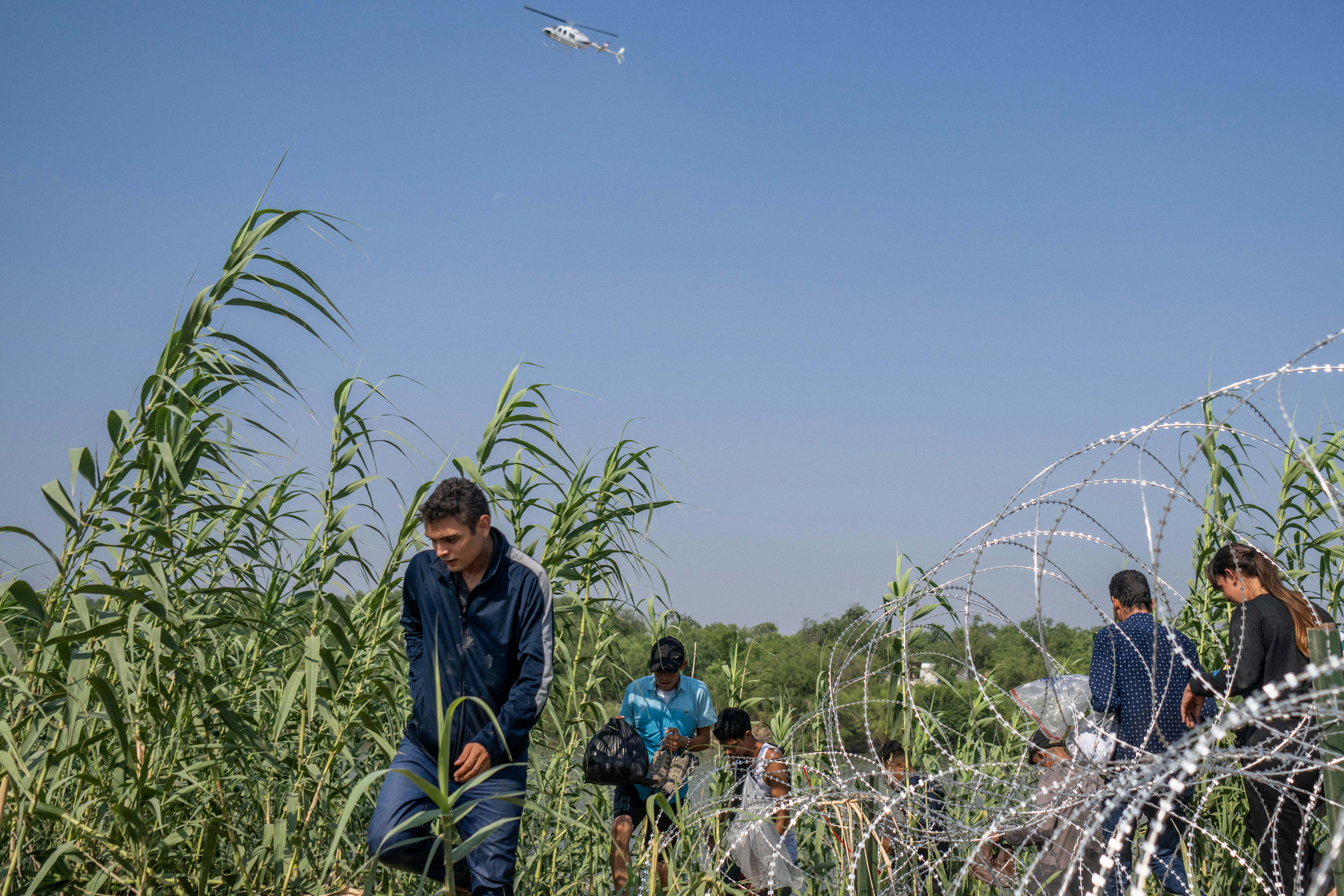 EAGLE PASS, TEXAS - MAY 21: Migrants from El Salvador walk through brush alongside the banks of the Rio Grande after crossing into the U.S. on May 21, 2022 in Eagle Pass, Texas. Title 42, the controversial pandemic-era border policy enacted by former President Trump, which cites COVID-19 as the reason to rapidly expel asylum seekers at the U.S. border, was set to officially expire on May 23rd. A federal judge in Louisiana delivered a ruling today blocking the Biden administration from lifting Title 42.  (Photo by Brandon Bell/Getty Images)