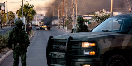 TOPSHOT - Mexicans soldiers stand guard near burning vehicles on a street during an operation to arrest the son of Joaquin 