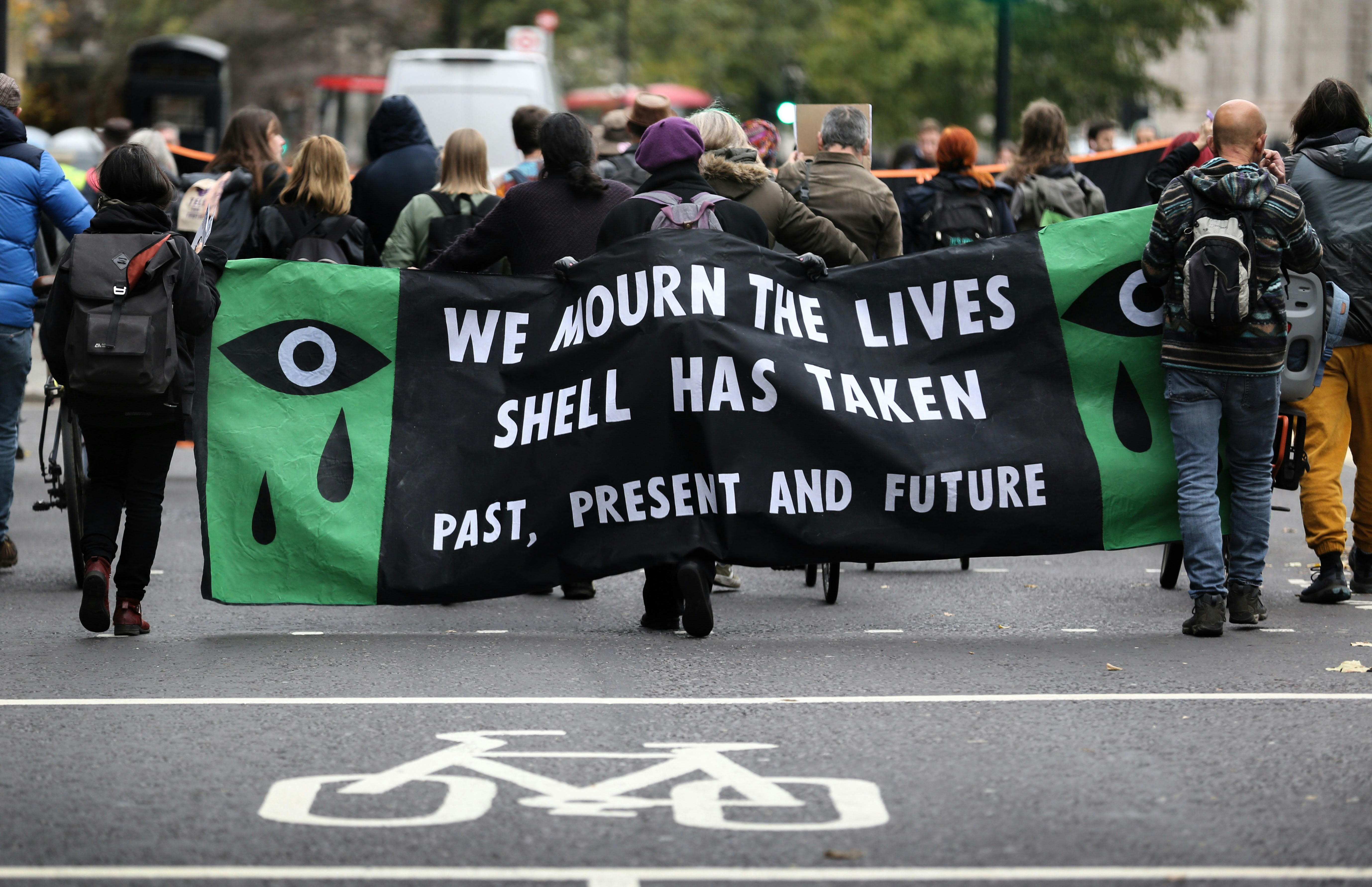 ЛОНДОН, АНГЛИЯ – 10 НОЕМВРИ: Протестиращите се събират зад транспарант против Shell, докато маршируват през Лондонското сити на 10 ноември 2022 г. в Лондон, Англия.  Това е 27-ата годишнина от екзекуцията на Ogoni 9, включително Ken Saro-Wiwa, в Нигерия за противопоставяне на Shell и техния бизнес с изкопаеми горива в делтата на Нигер.  Extinction Rebellion изправя Vanguard на съд, тъй като протестиращите смятат, че инвестирането им в компании за изкопаеми горива е неетично.  (Снимка от Мартин Поуп/Гети изображения)