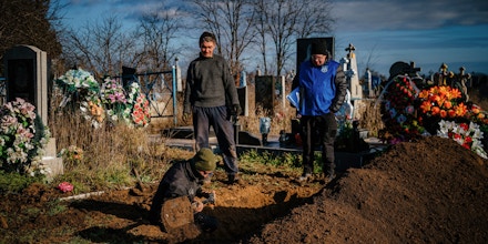 A war crimes prosecutor (R) stands next to local residents digging up a grave to collect the remains of Nadiya Medvidyiva, 58-year-old, killed on September 18, 2022 during the Russian invasion, at the cemetery of Pravdyne, near Kherson, southern Ukraine, on December 29, 2022. (Photo by Dimitar DILKOFF / AFP) (Photo by DIMITAR DILKOFF/AFP via Getty Images)